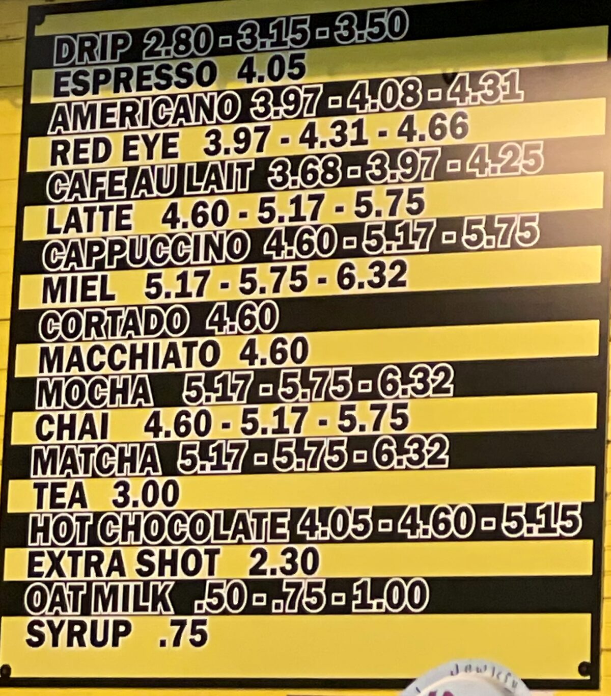 The Daily Bird's yellow and black menu board listing drink prices